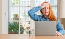 Redhead Woman Using Computer Laptop At Home Stressed With Hand On Head, Shocked With Shame And Surprise Face, Angry And Frustrated. Fear And Upset For Mistake.